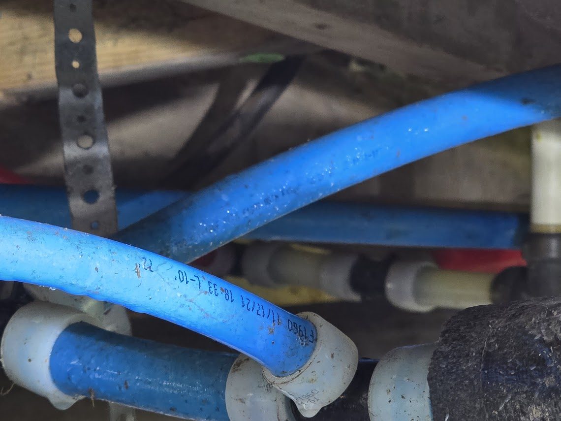 New PEX water lines run on hangers under a pier-and-beam house in Anahuac, alongside the original drain lines