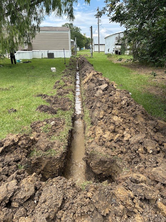 Open trench across a yard in Anahuac with new sewer line laid in before backfill