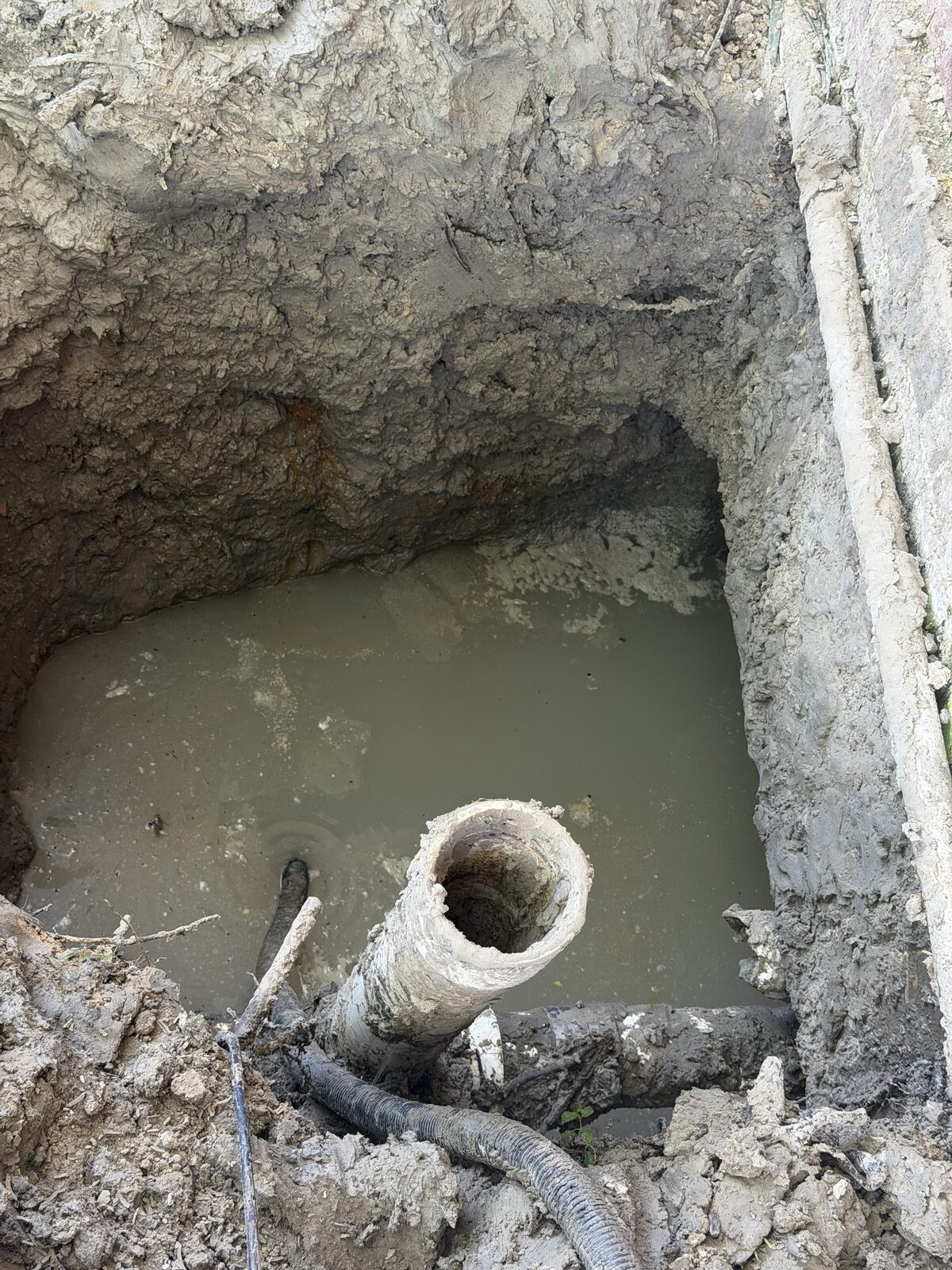 A broken sewer pipe exposed in a water-filled excavation