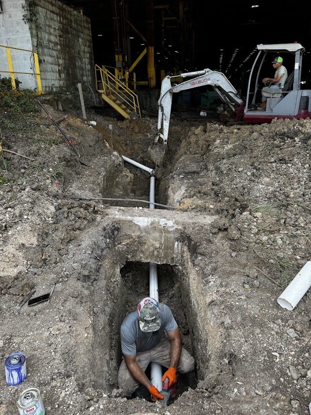 Mini excavator and technician tunneling under a building footing for a commercial sewer line replacement