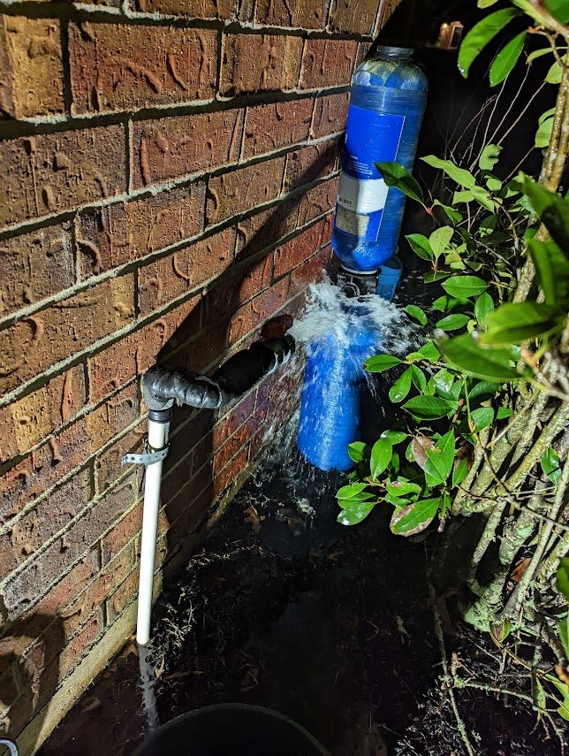 Water gushing from a broken line at the brick of a house at night