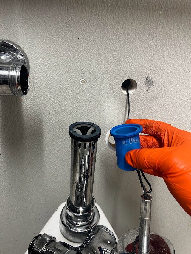 Gloved hand pulling the vacuum breaker out of a commercial flushometer during a repair