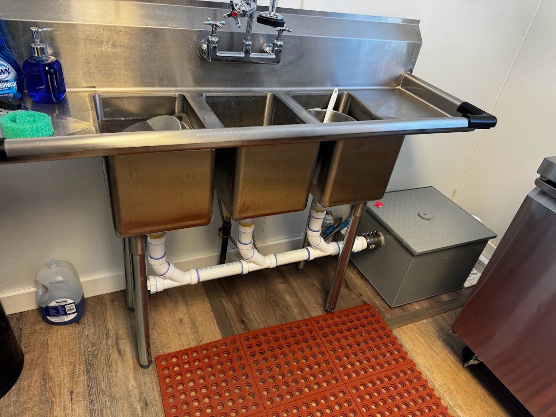 Under-sink grease trap plumbed to a three-compartment commercial kitchen sink