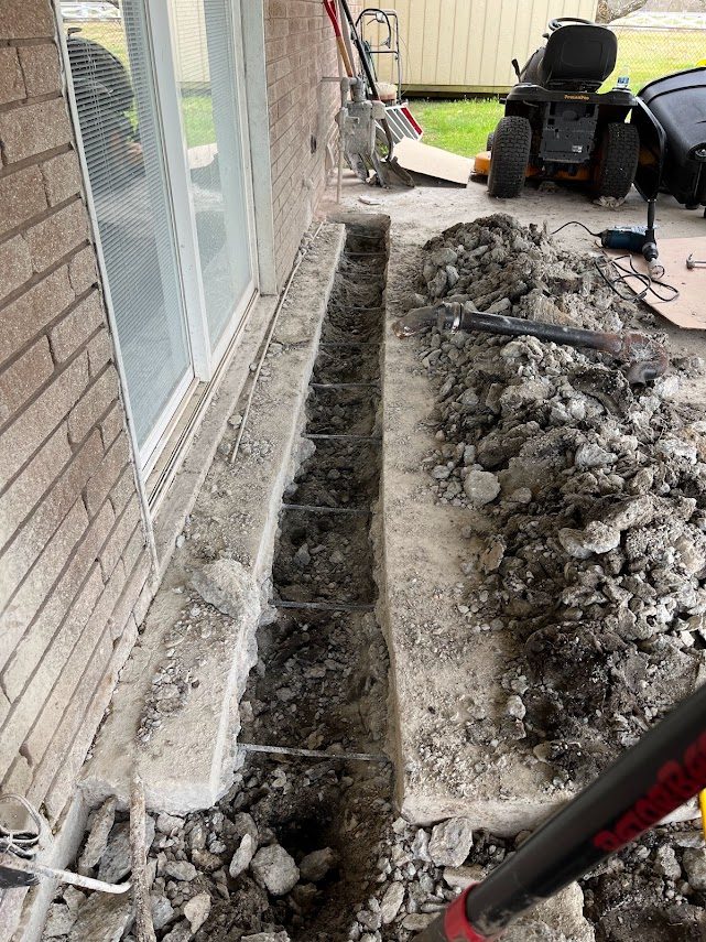 Slab cut along a foundation with rebar exposed for a washing machine drain reroute in Old River-Winfree