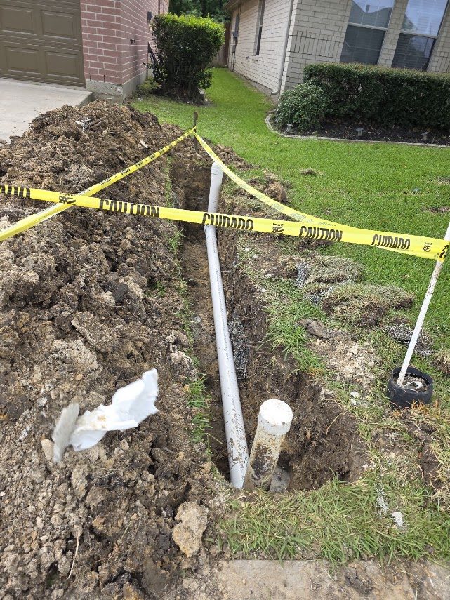 Roughly fifteen feet of residential sewer line replaced in a yard, caution tape around the excavation
