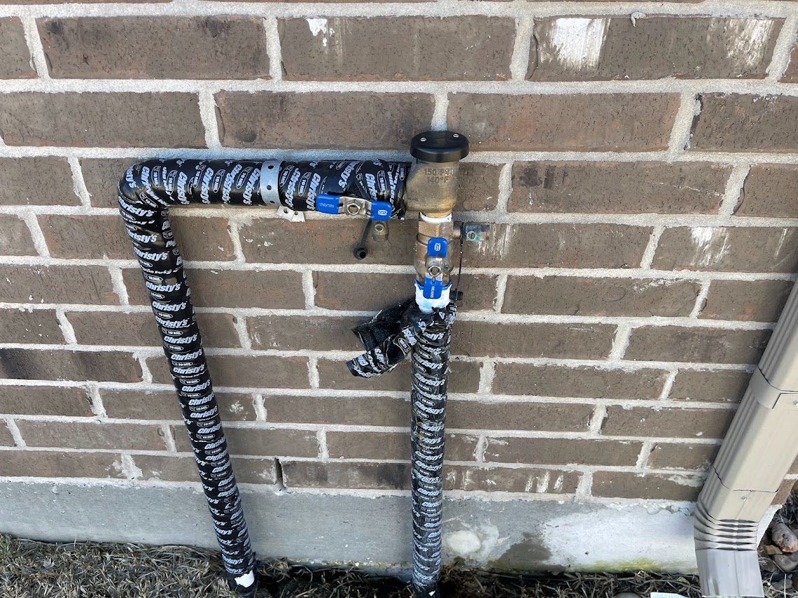 Sprinkler system backflow unit wrapped and mounted on a brick wall