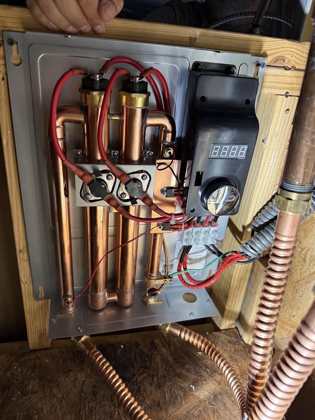 Electric tankless water heater opened for repair showing heating elements and copper manifold