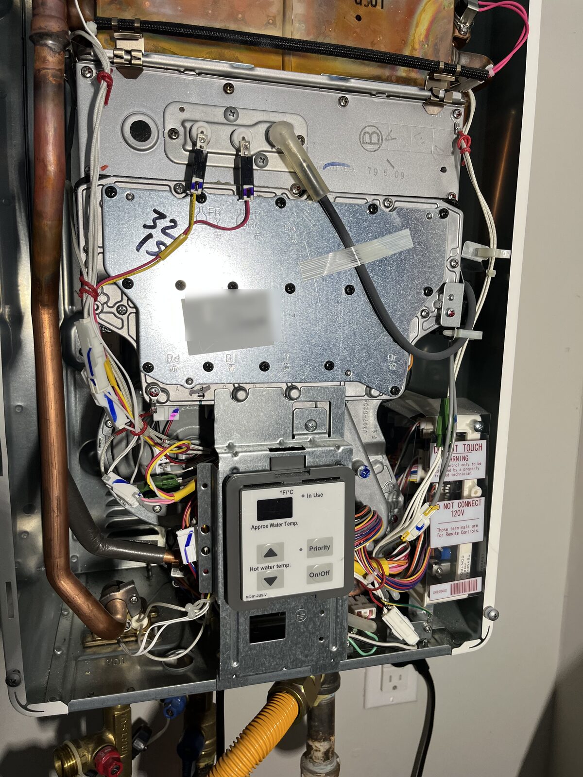 Inside a gas tankless water heater during a warranty repair, control board and wiring visible