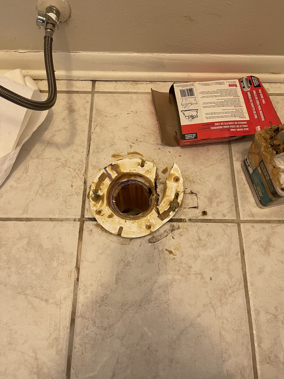Broken plastic toilet flange in a tile floor with the toilet removed
