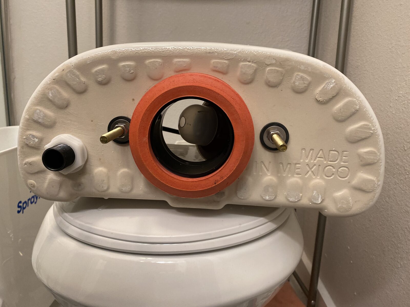 Underside of a rebuilt toilet tank showing a new orange gasket and new brass bolts