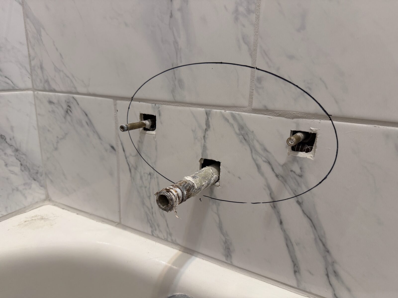 Tub valve rough-in cut through marble tile with the marker circle still drawn on the tile