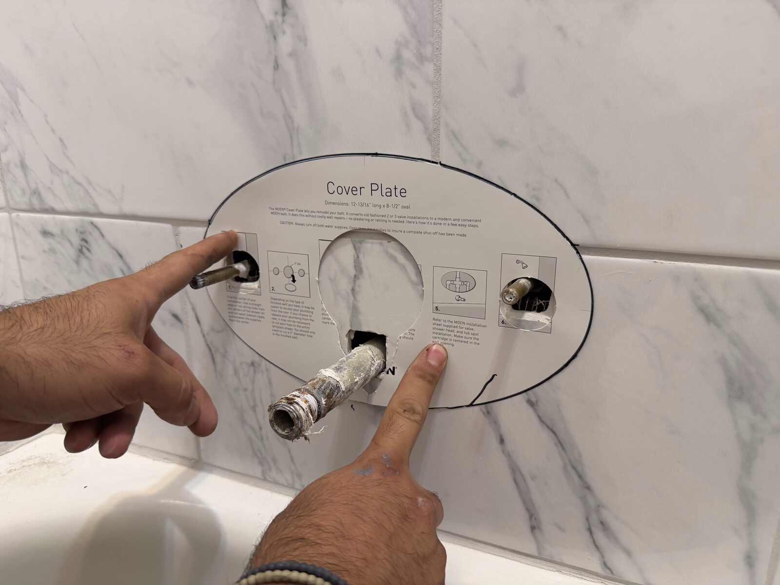 Moen cover plate template held against the tile to check the opening will be covered