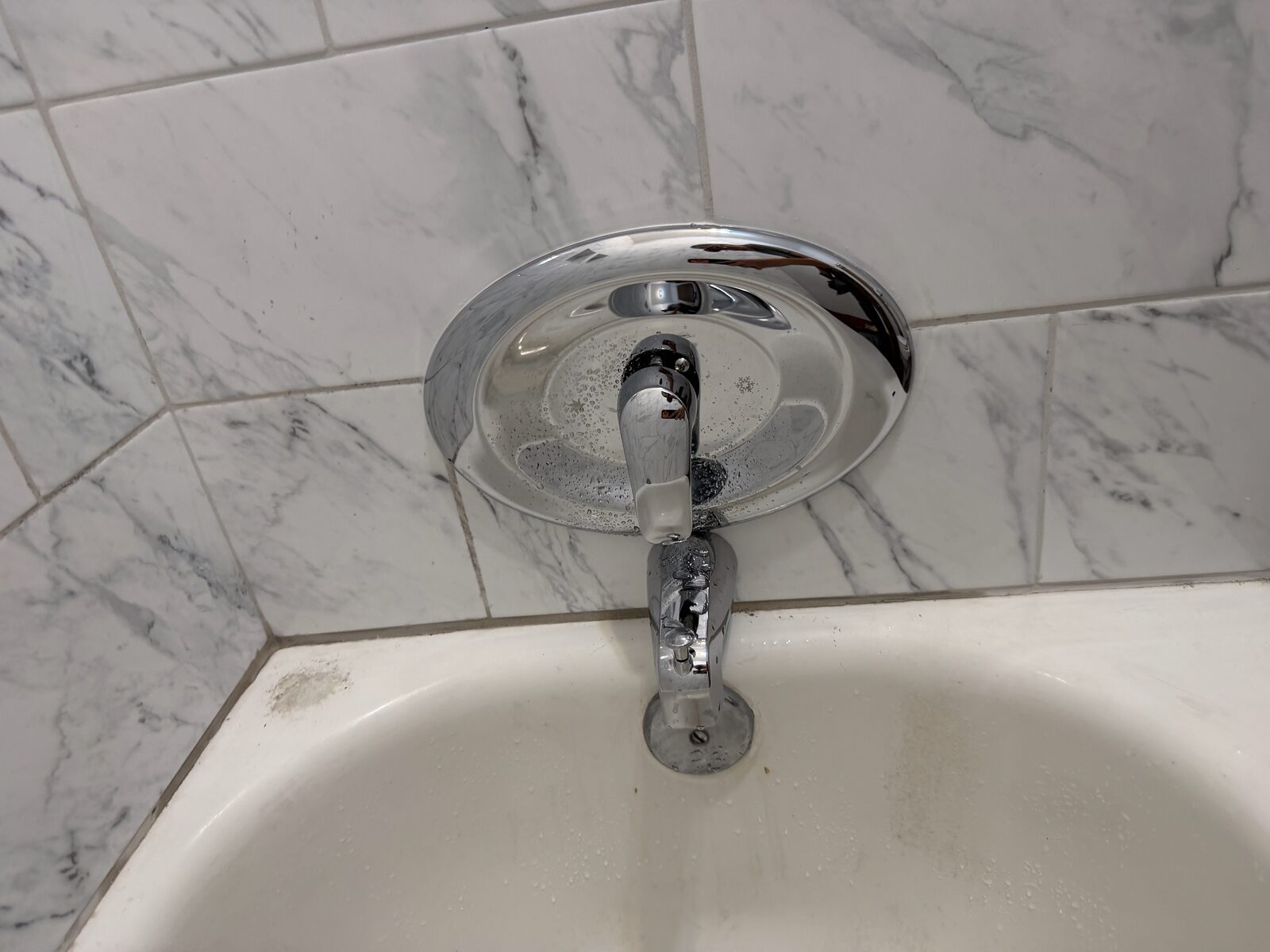 Finished single-lever tub valve with the escutcheon covering the opening in the tile