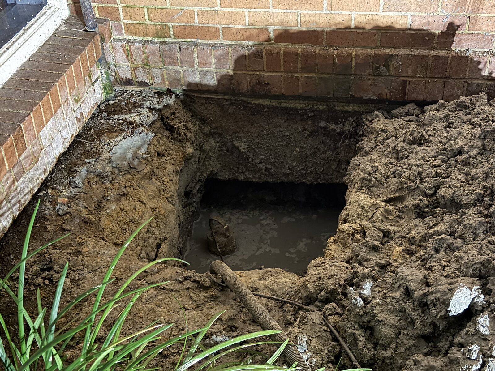 Tunnel entrance excavated under a slab beside a brick wall