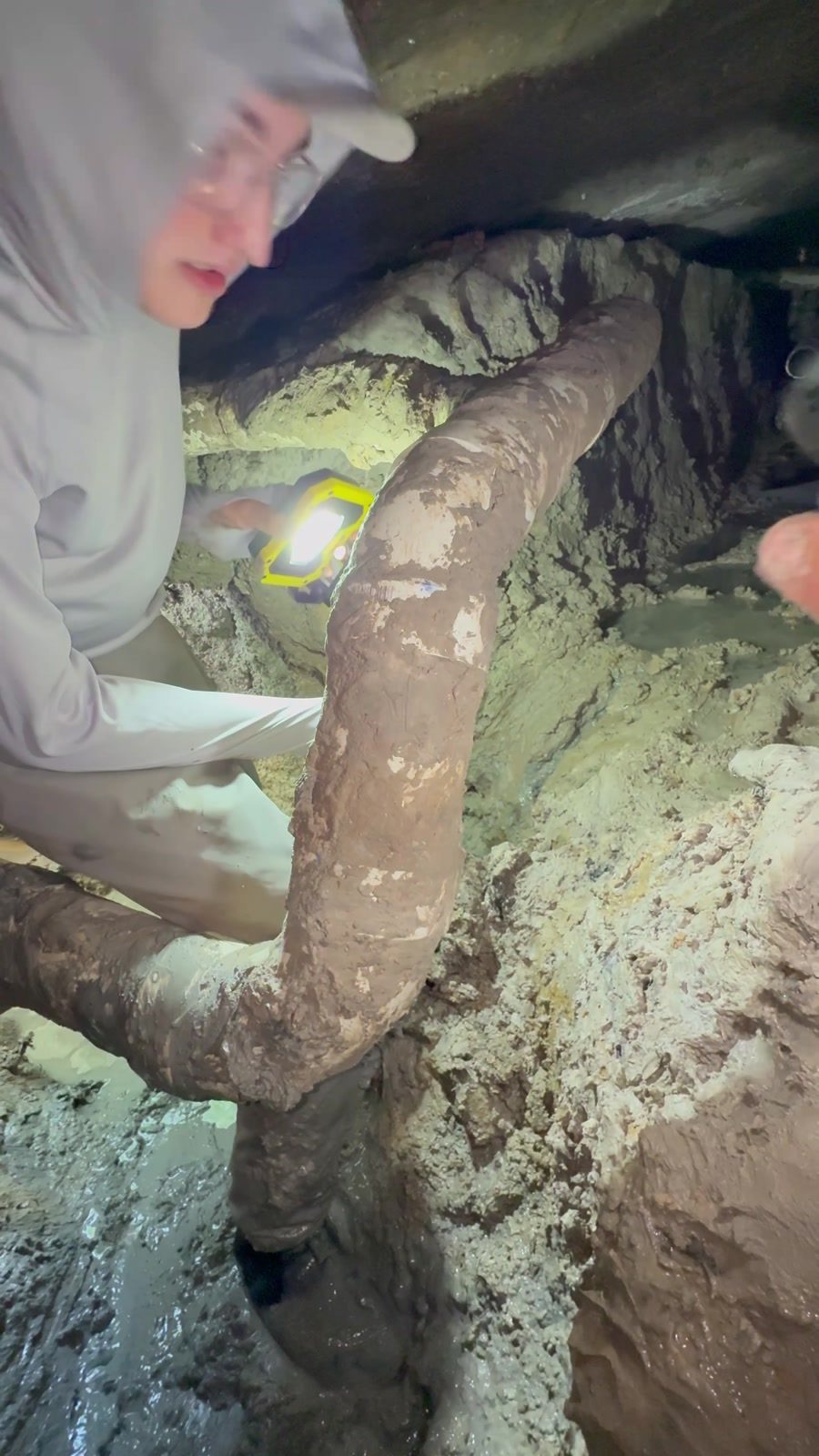 Technician working on an old cast iron drain line inside an under-slab tunnel